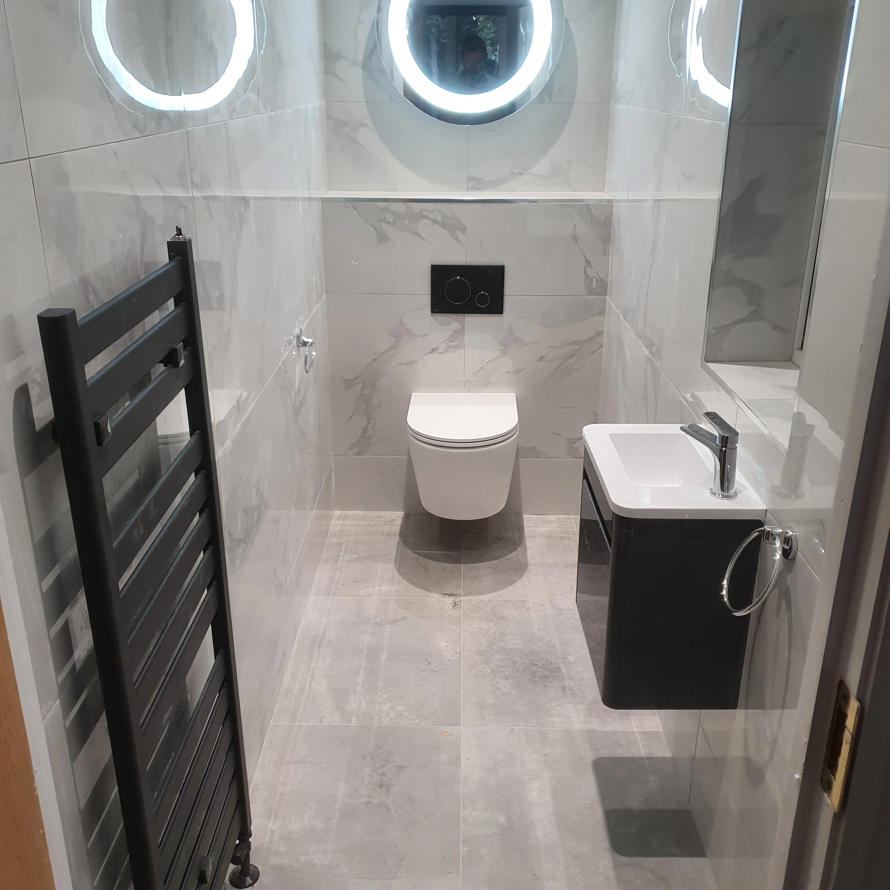 Modern small bathroom with wall-mounted toilet, black towel radiator, and a compact sink with a mirror above.