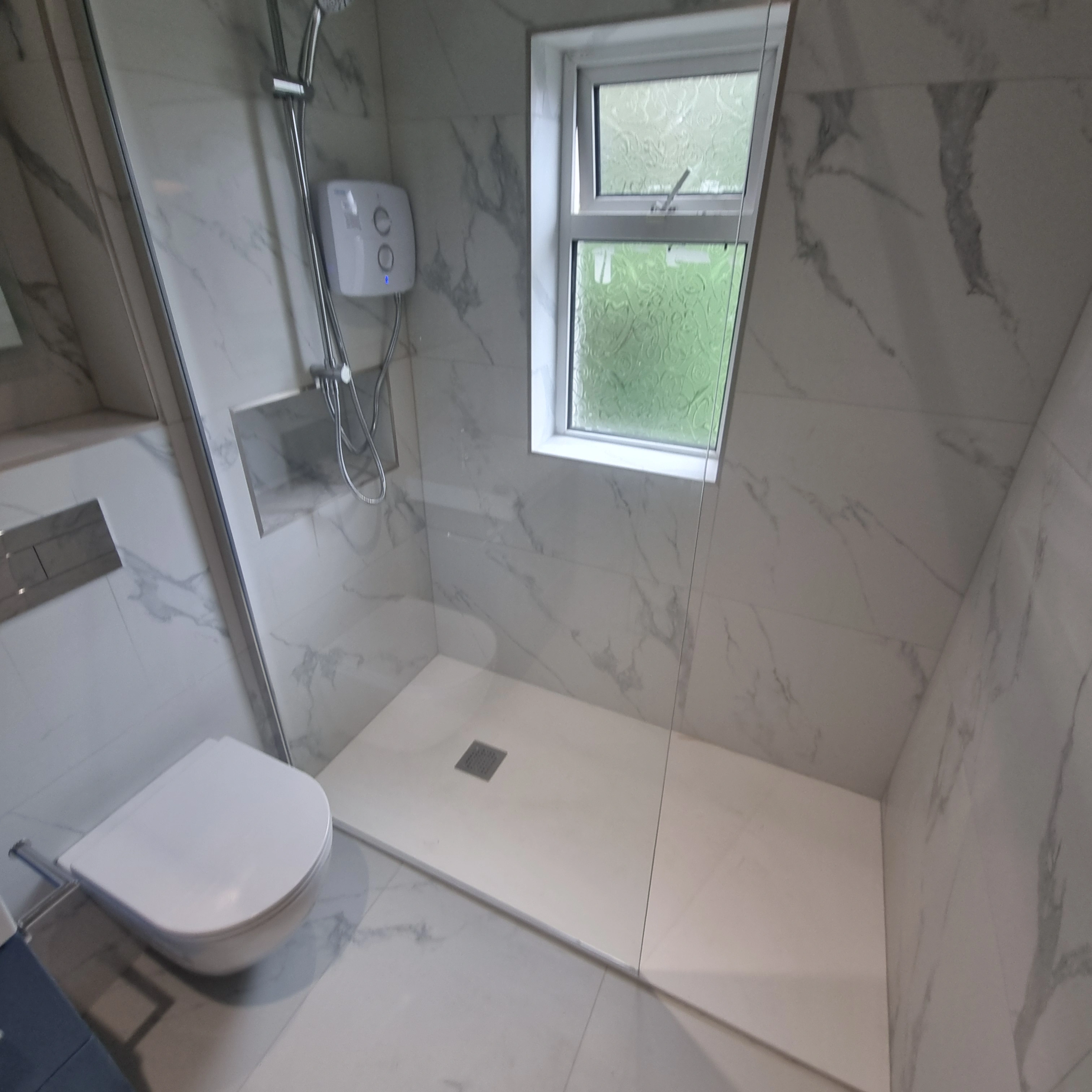 Modern bathroom with white marble walls, a walk-in shower with a handheld showerhead, and a wall-mounted toilet.