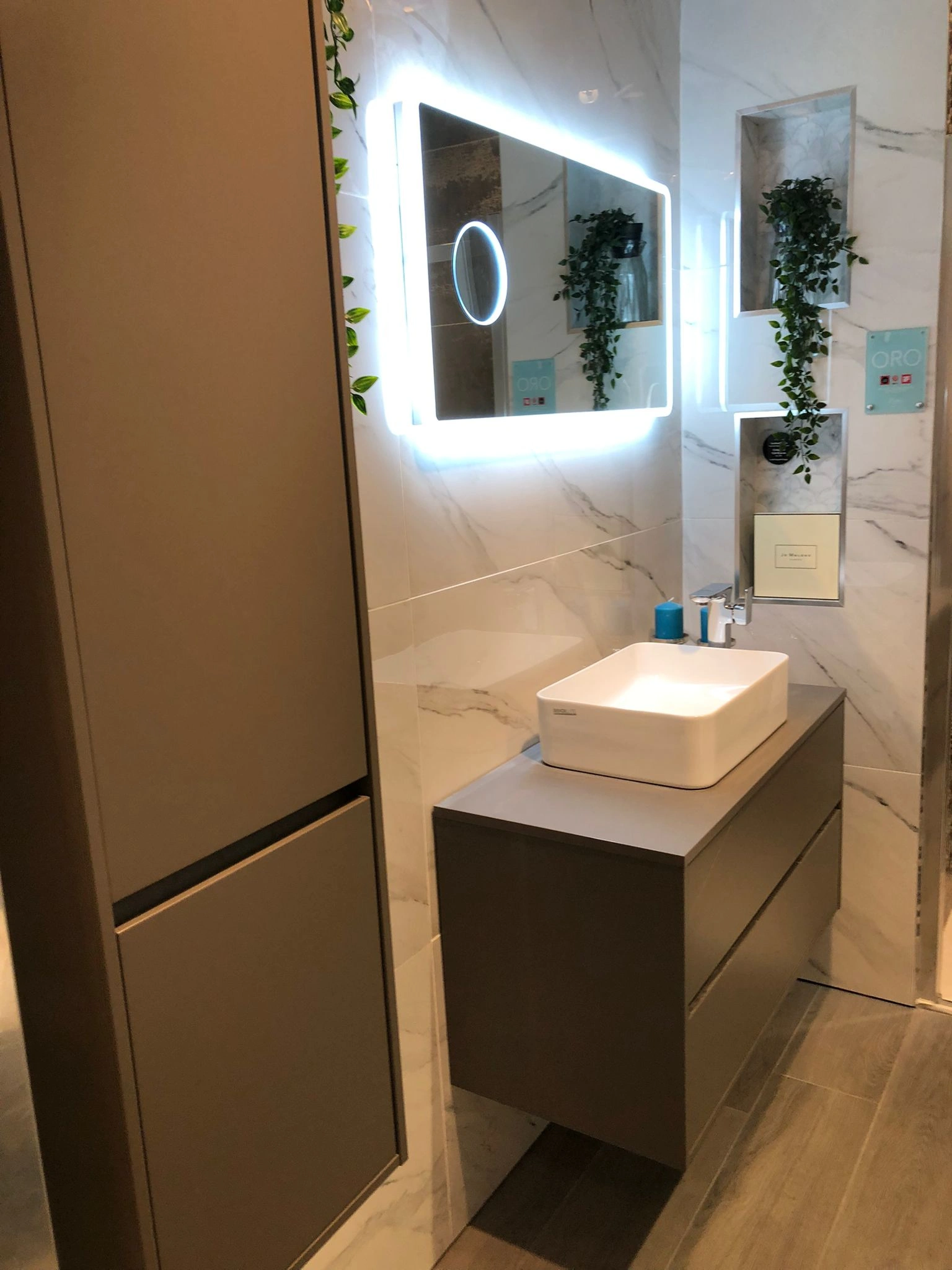 Modern bathroom with a floating gray vanity, white rectangular sink, illuminated rectangular mirror, and plants in built wall niches.