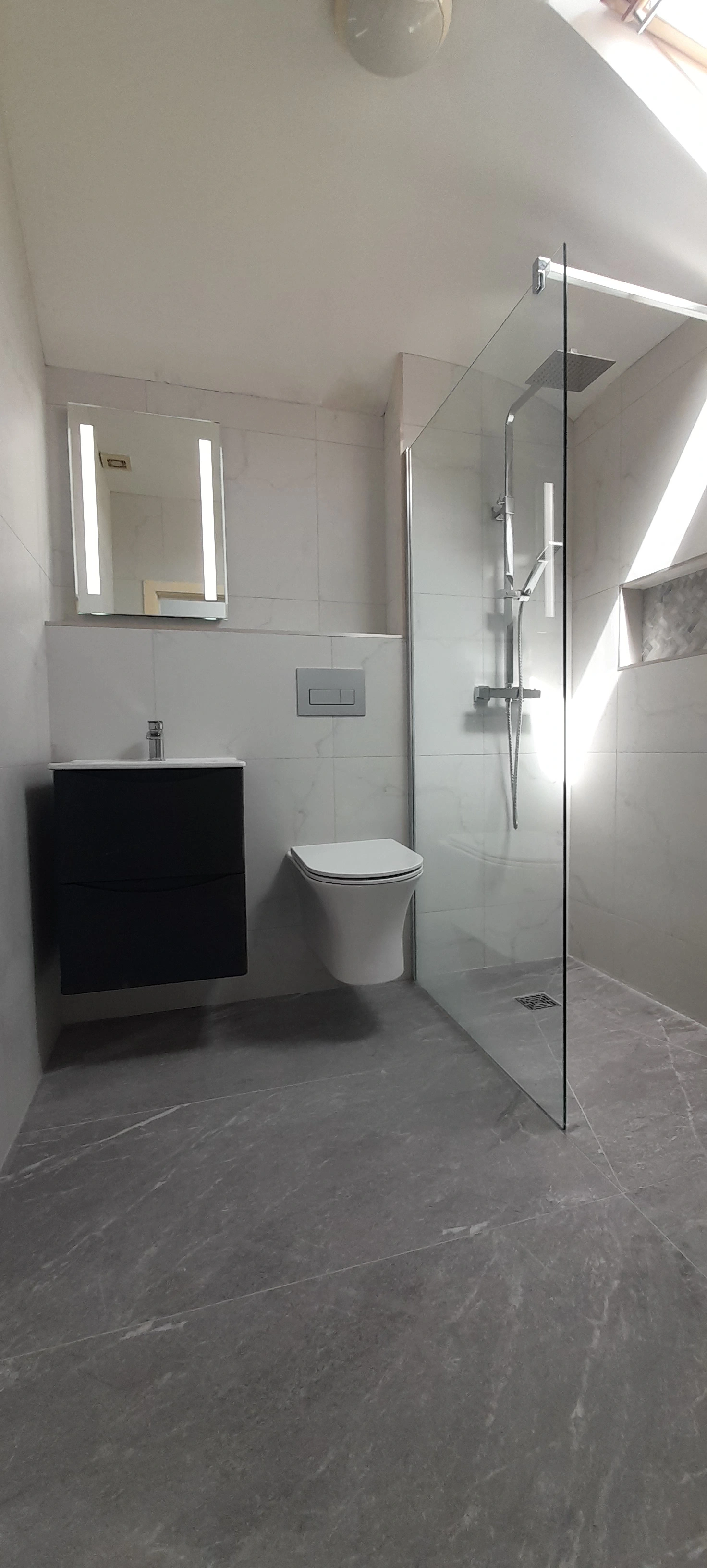 Modern bathroom with a floating toilet, black vanity with sink, illuminated mirror, and glass shower enclosure with rain showerhead.