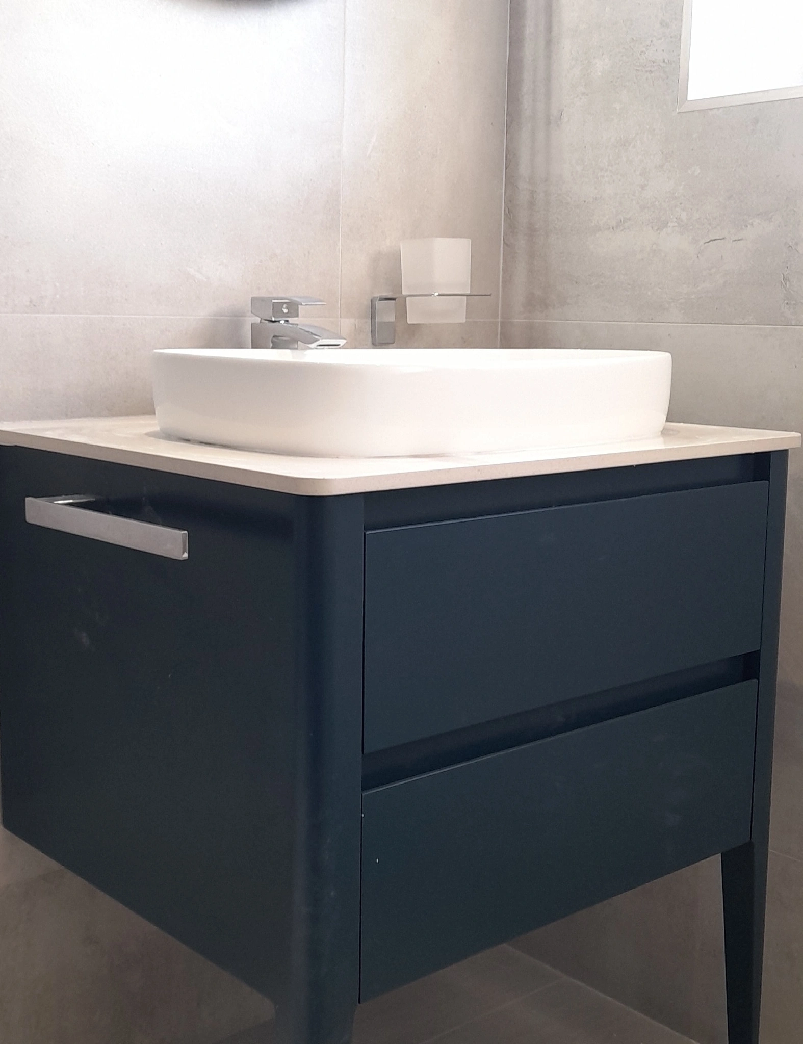 Modern bathroom sink with white rectangular basin on a dark blue vanity cabinet with drawers.