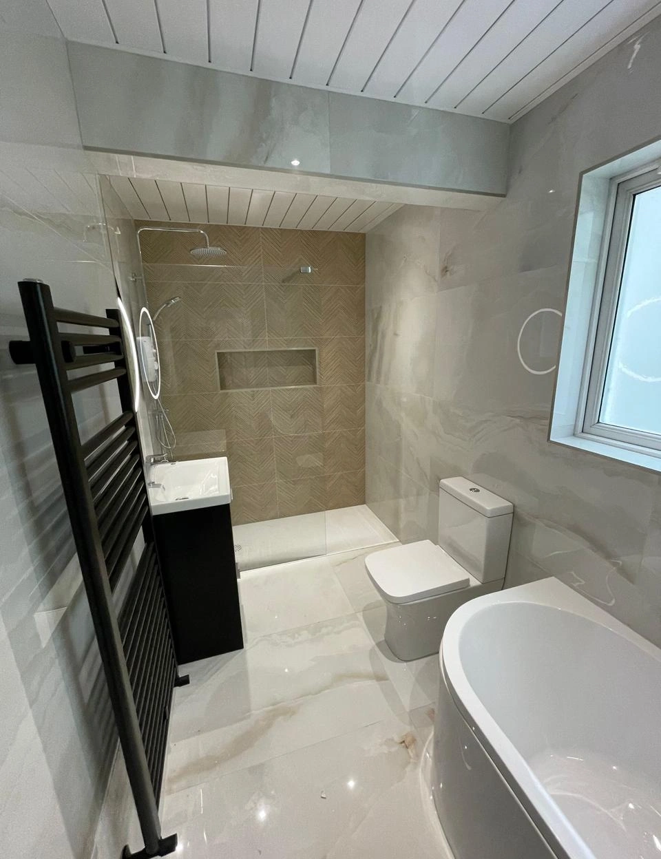 Modern bathroom with a white bathtub, a toilet, a black vanity sink, a glass-enclosed shower with wood-pattern tiles, and a black heated towel rail.