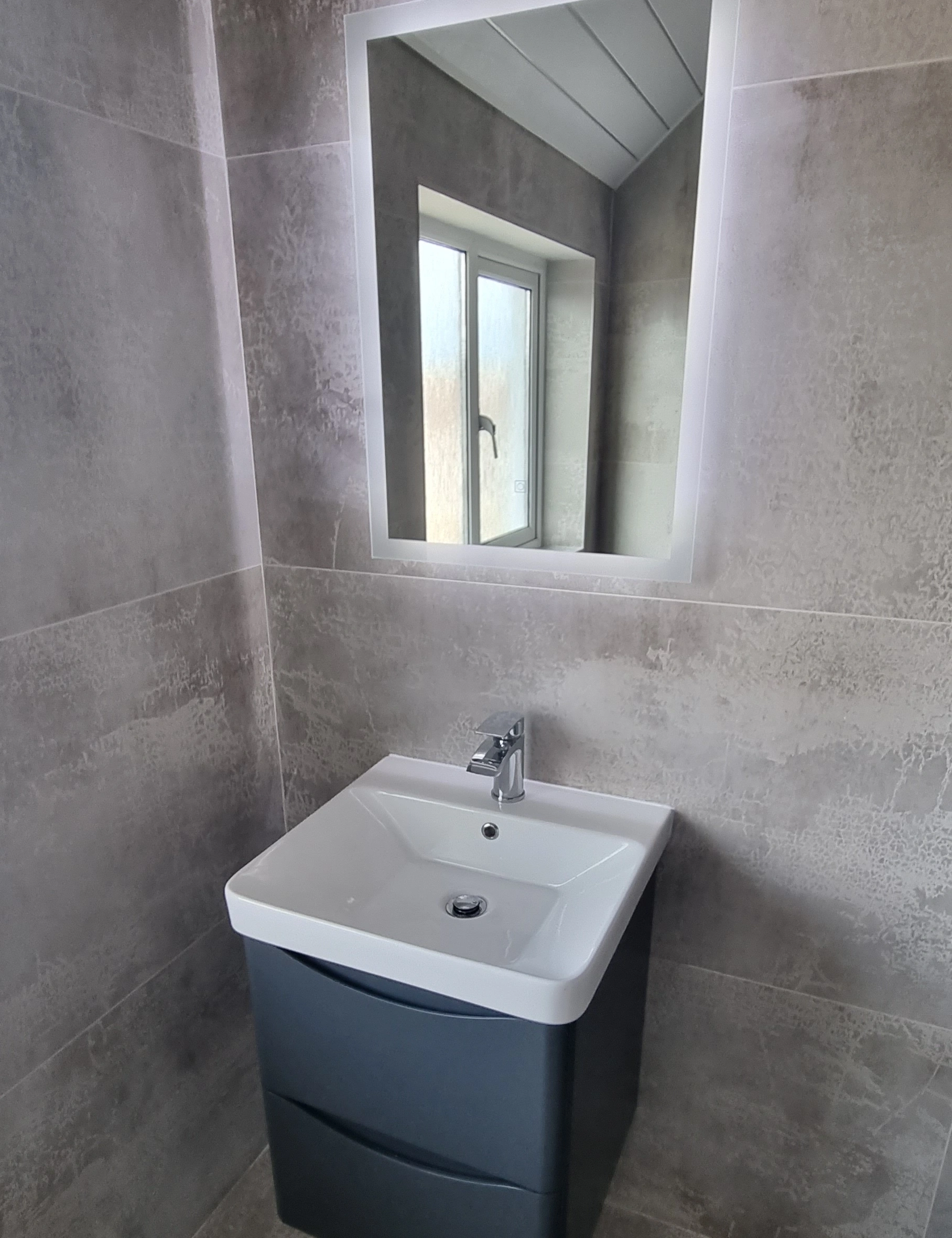 Modern bathroom sink with white basin, chrome faucet, dark cabinet, and square mirror