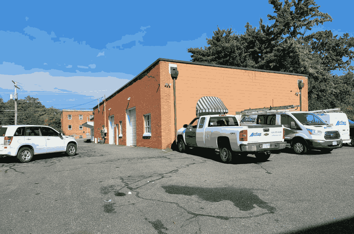 Parking lot beside a single-story brick building with white garage doors and three white vehicles, two with Airflow company logos.