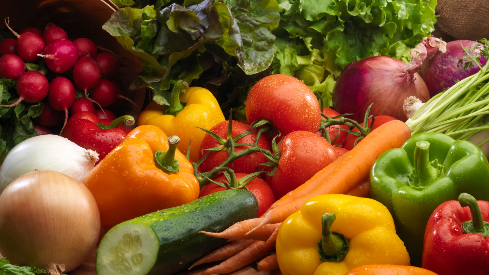 A vibrant assortment of fresh vegetables, including tomatoes, bell peppers, radishes, carrots, and leafy greens, conveying a sense of healthy abundance.