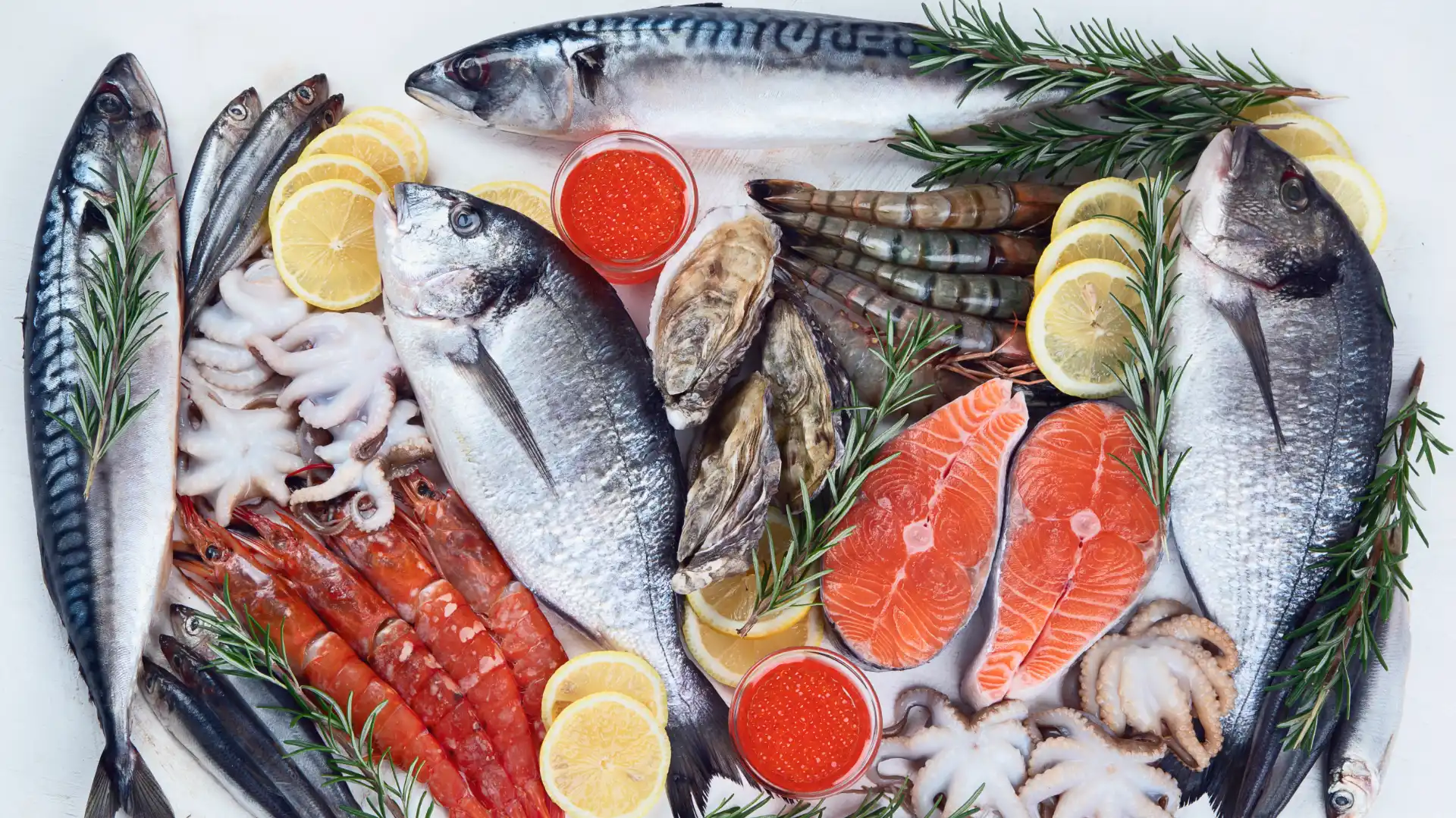 An assortment of seafood including fish, shrimp, octopus, and oysters is elegantly arranged with lemon slices, sprigs of rosemary, and red caviar.