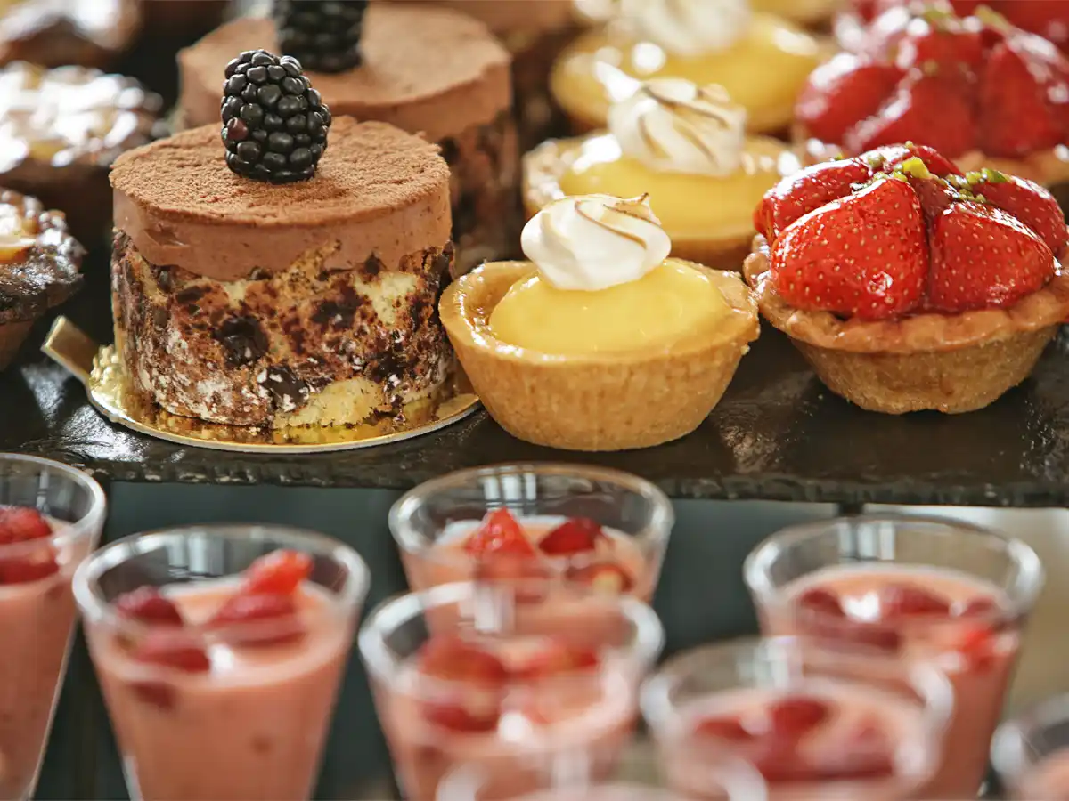 A delectable display of desserts featuring chocolate cake topped with a blackberry, lemon tarts with cream, and strawberry tarts, exuding a fresh, indulgent vibe.