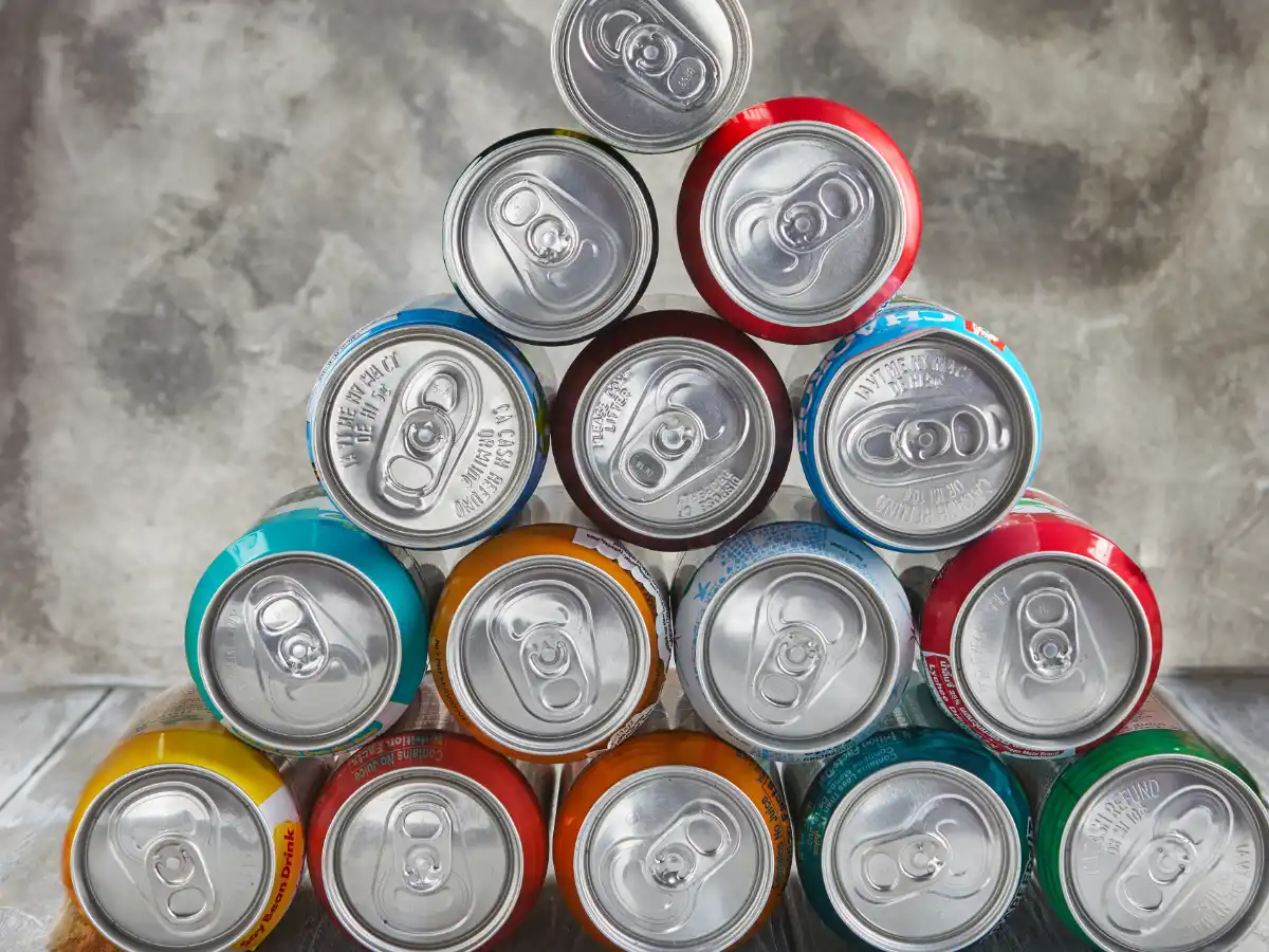 A pyramid of various colourful soda cans viewed from the top, arranged against a grey textured background. The setup conveys a neat and organized appearance.