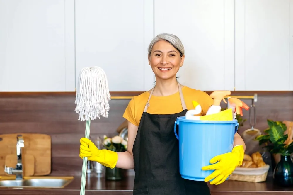 Smiling house cleaner holding a bucket and mop, ready to start a home cleaning service.