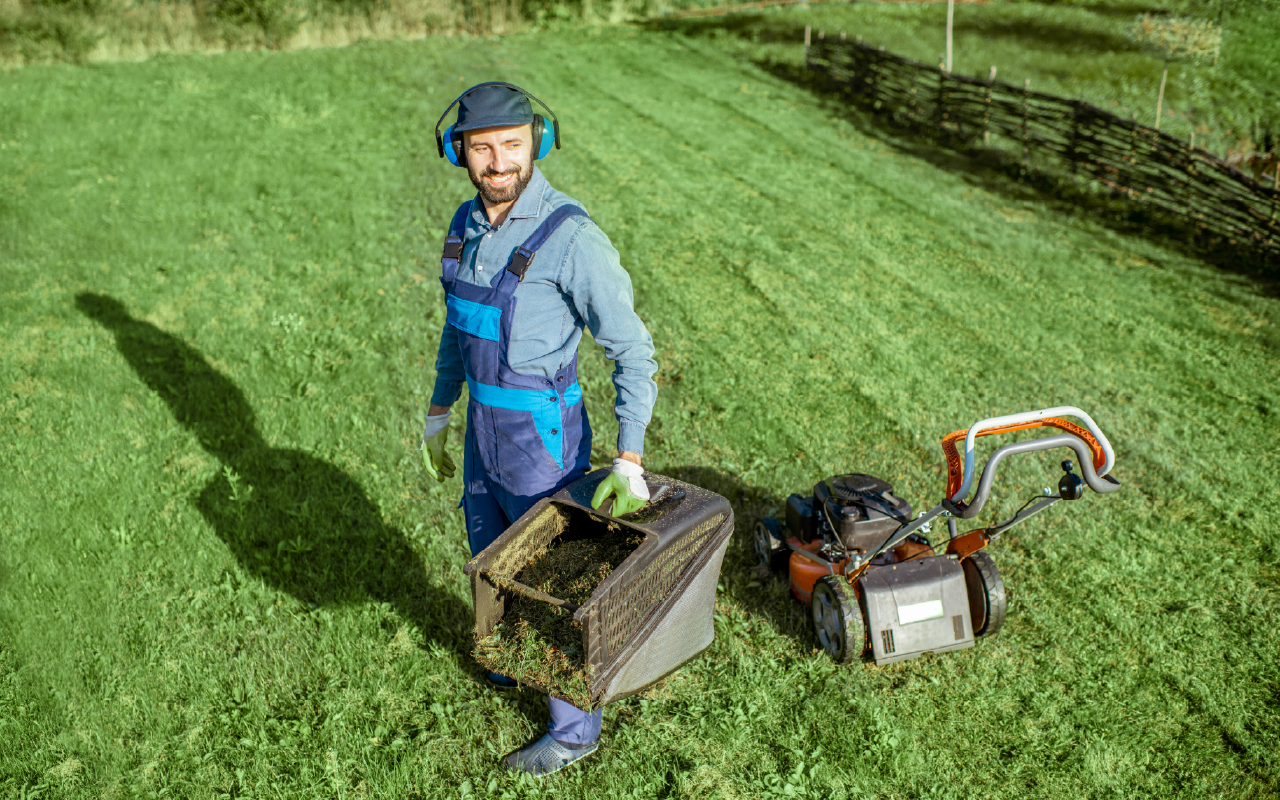 Worker carrying yard tools on a sunny lawn, representing outdoor cleanup and maintenance services.