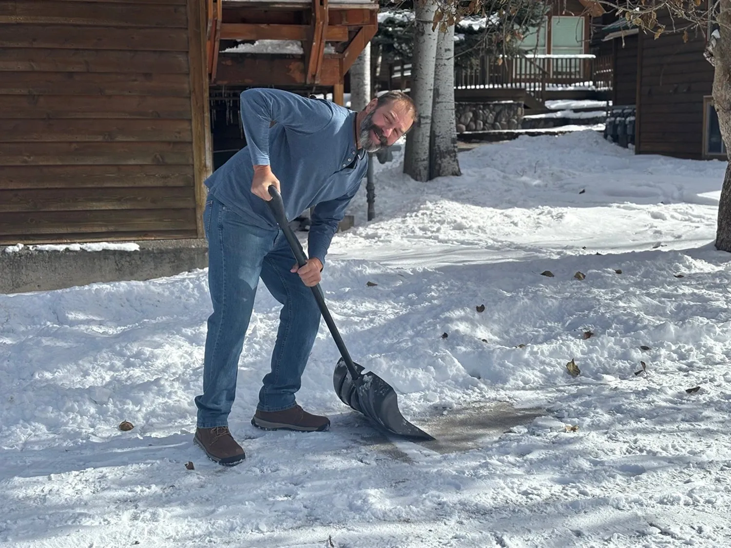 A Lucky Services team member smiling while shoveling snow outside a cabin in Ouray, Colorado — representing reliable local help for winter home services.
