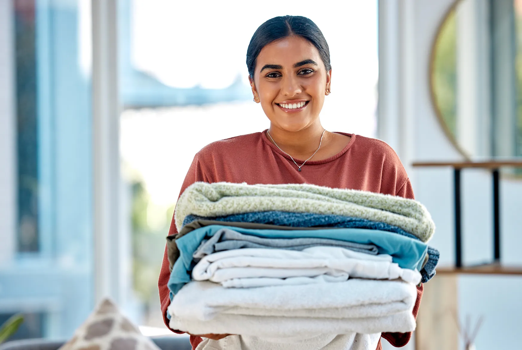 Smiling Lucky Services team member holding a stack of clean, folded linens — representing professional vacation rental turnover service in Ridgway, Colorado.