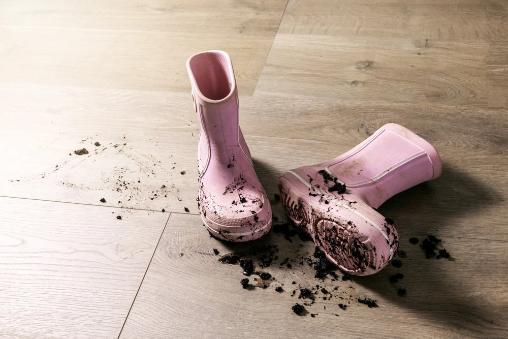 Muddy pink rain boots on a hardwood floor symbolizing Lucky Services’ deep cleaning and window washing during Durango’s spring mud season.