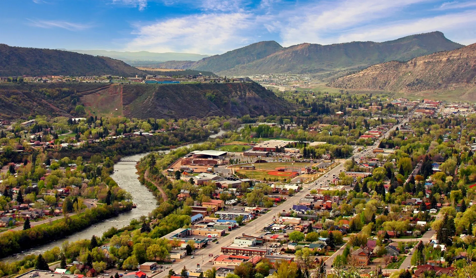 Aerial view of downtown Durango, Colorado, with the Animas River winding through the valley and mountains in the background.