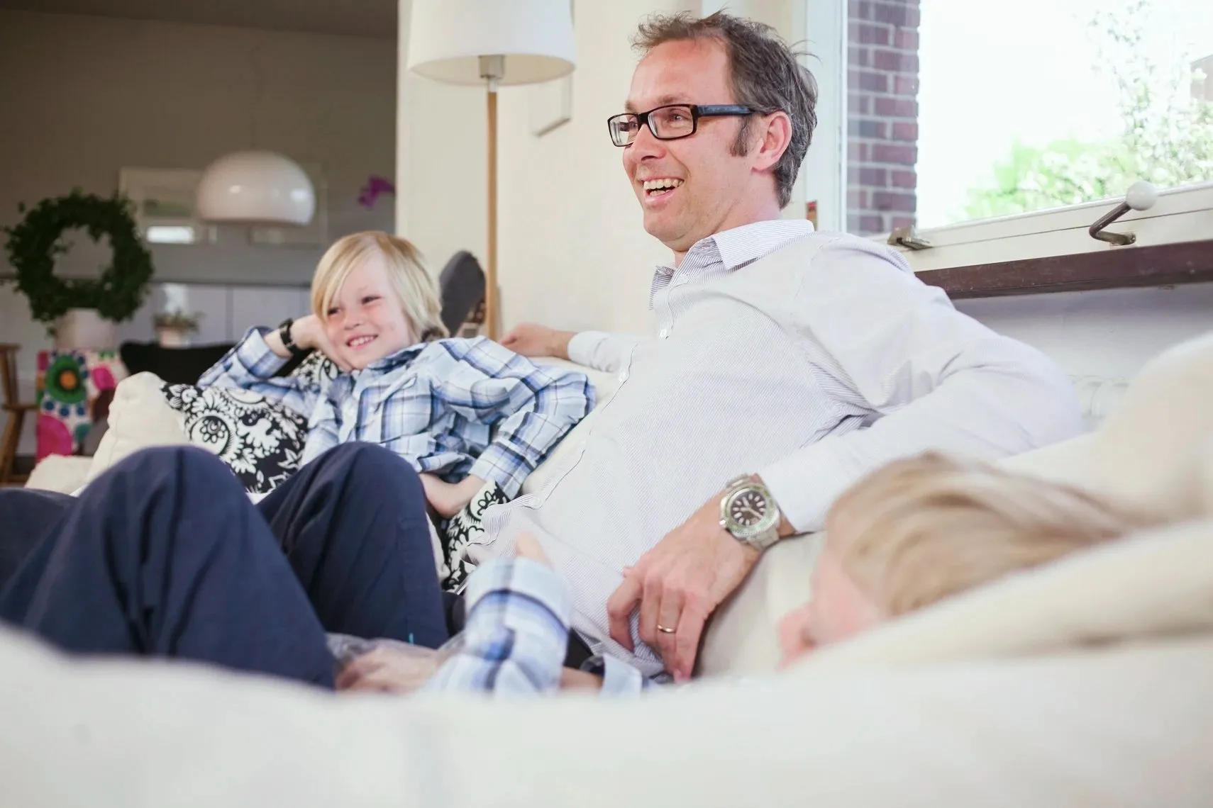 Father relaxing on a couch, laughing with his two children at home.