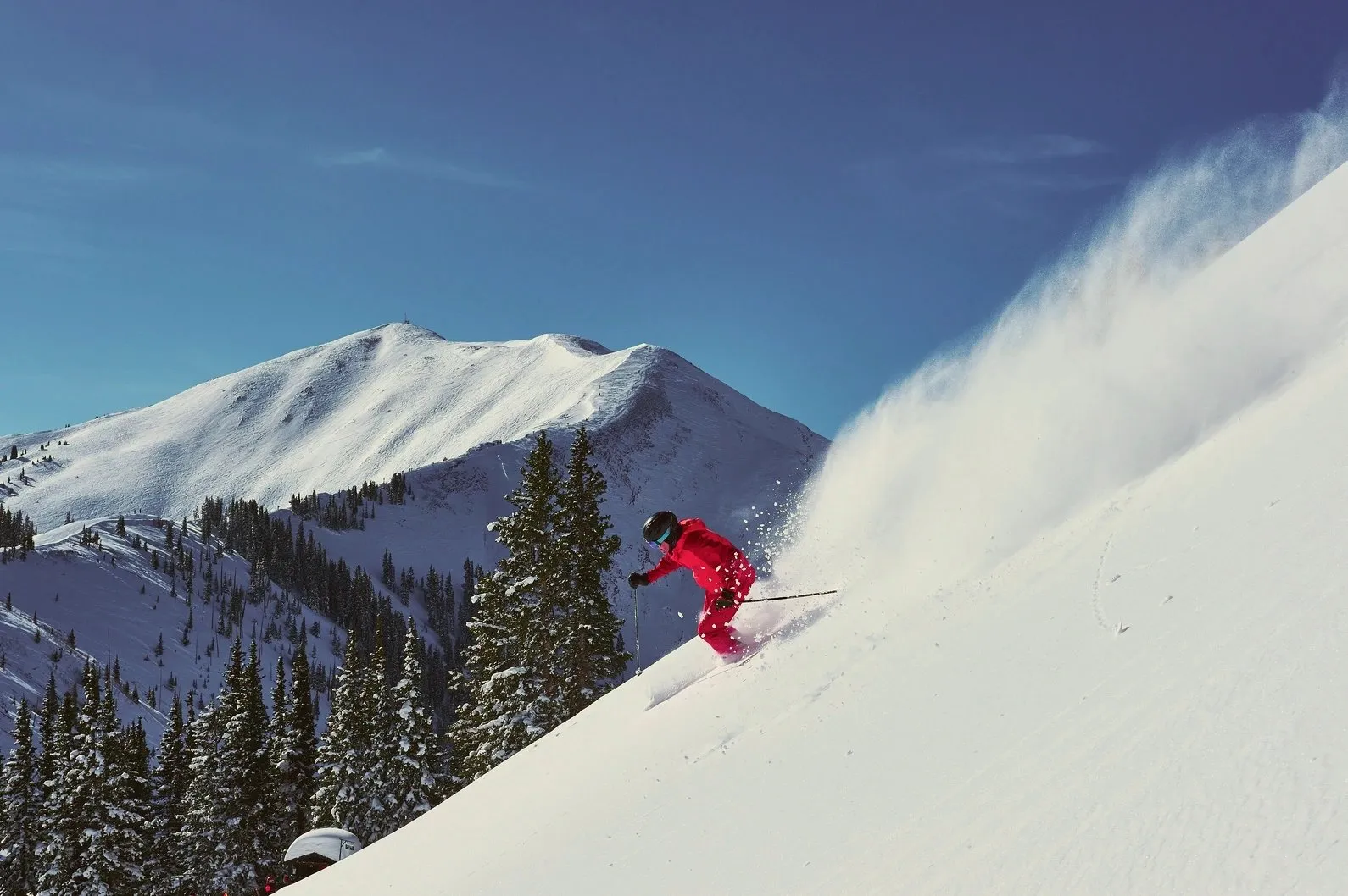 Skier carving through fresh powder on a snowy Colorado mountain slope.