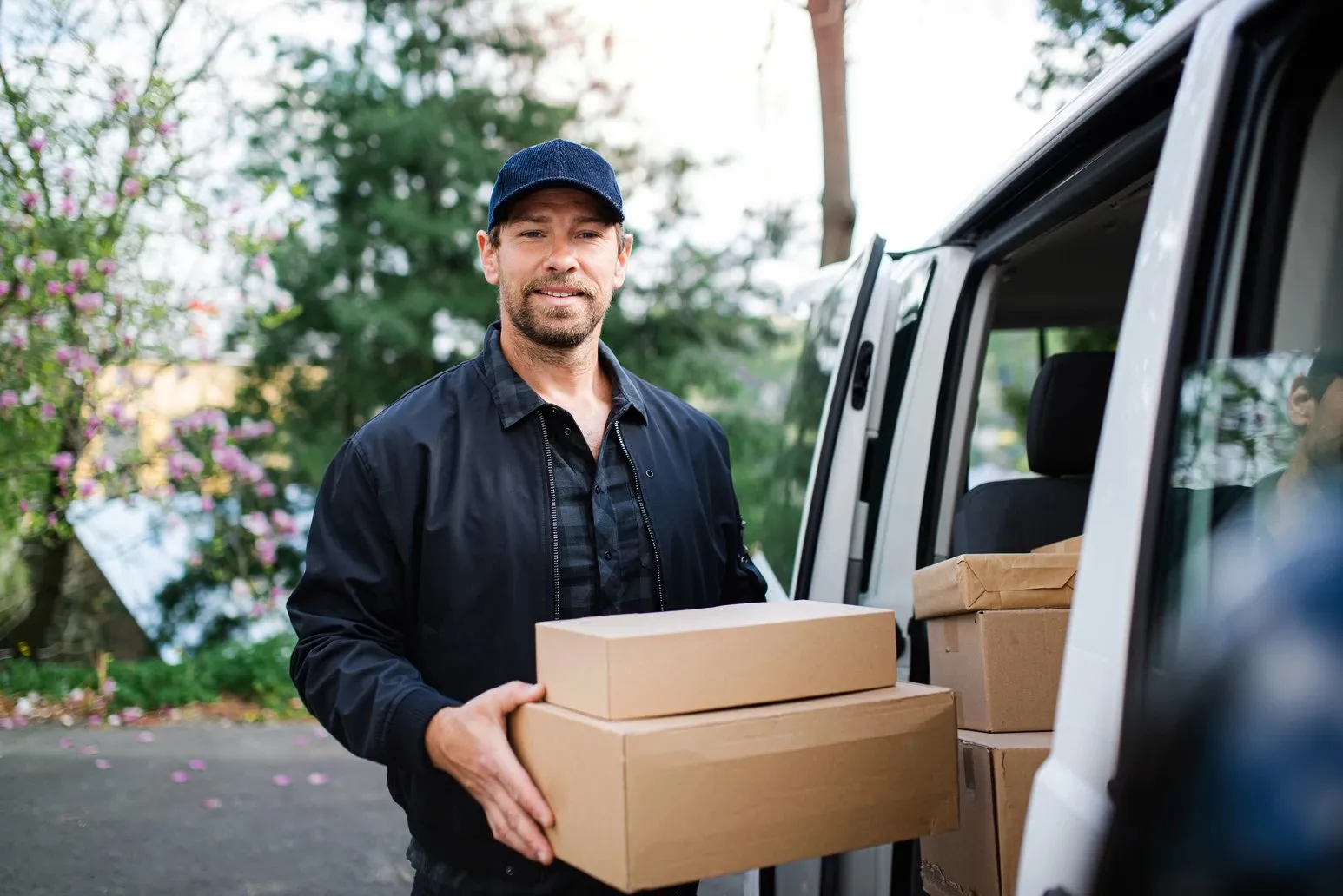 Smiling delivery driver carrying packages from his van.
