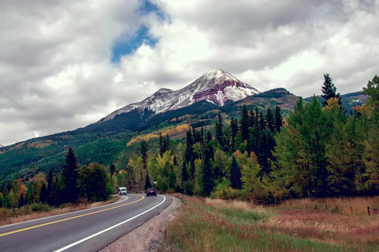 Scenic mountain highway view with a snow-capped peak and evergreen forest in Southwest Colorado.