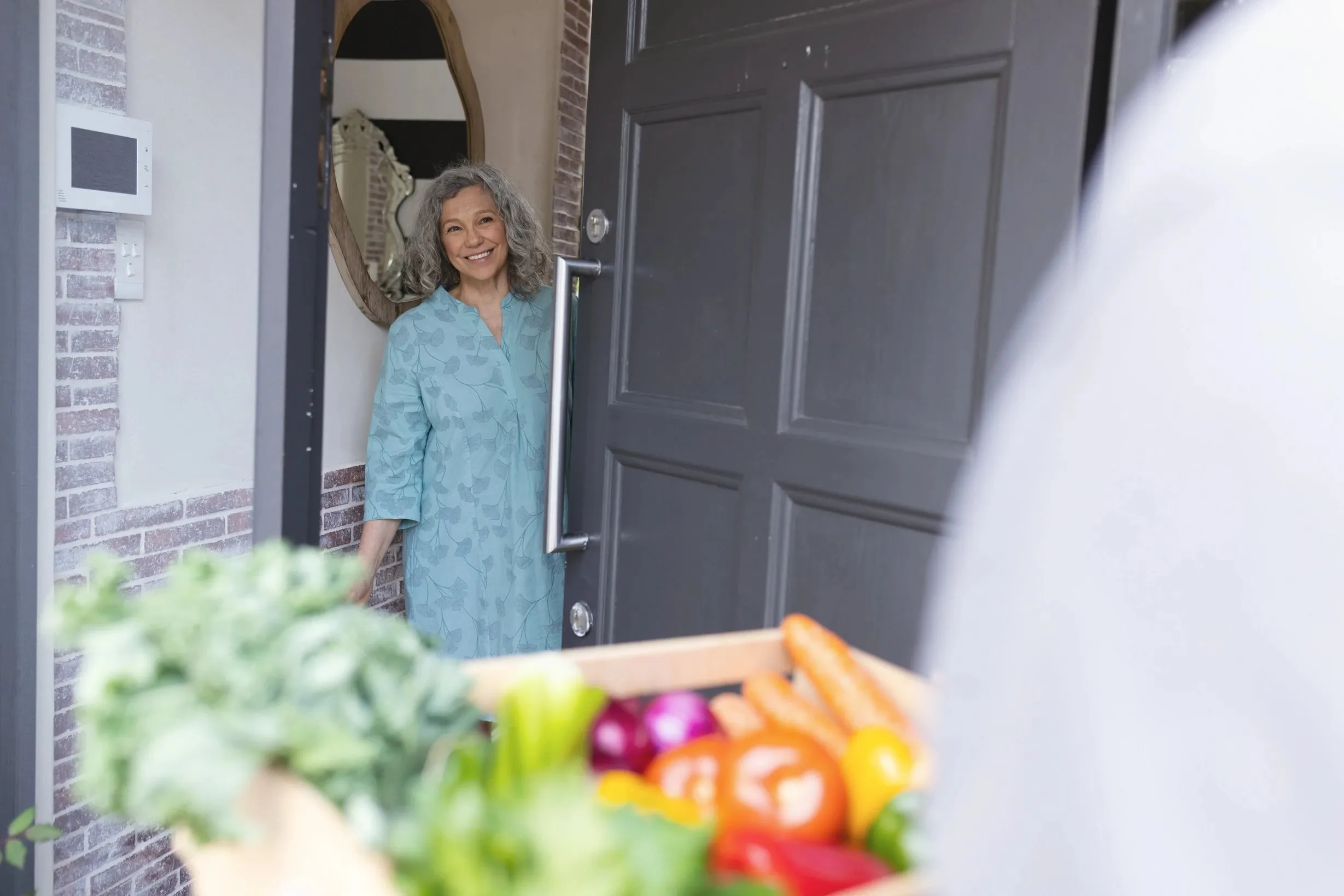 Smiling woman receiving a box of fresh grocery delivery at her front door.