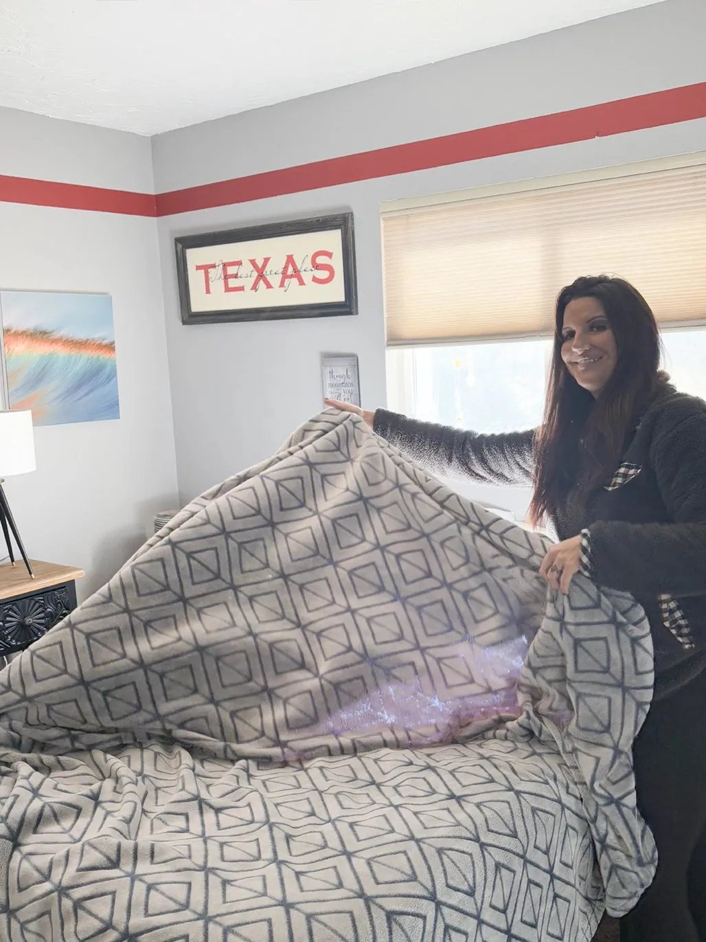 Woman making a bed with a patterned blanket in a tidy, decorated bedroom.