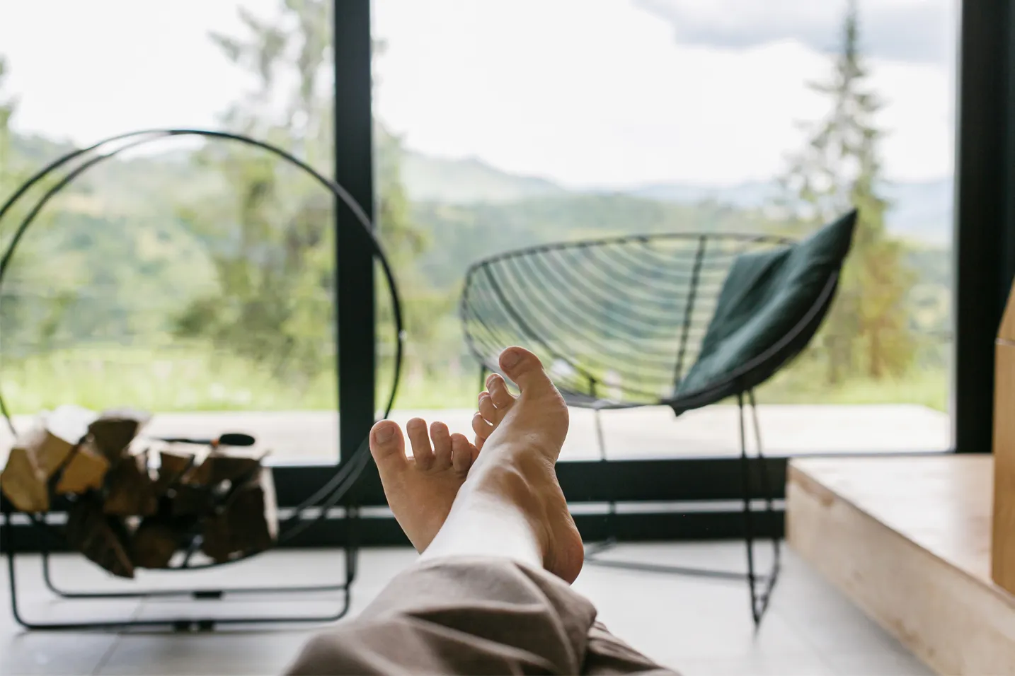 Bare feet propped up on an ottoman inside a bright home with mountain views through large windows â relaxing after the work is done.