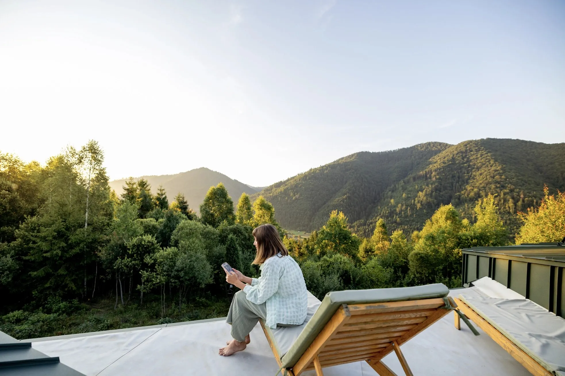 Woman relaxing on a deck chair, taking in a mountain and forest view at sunset.