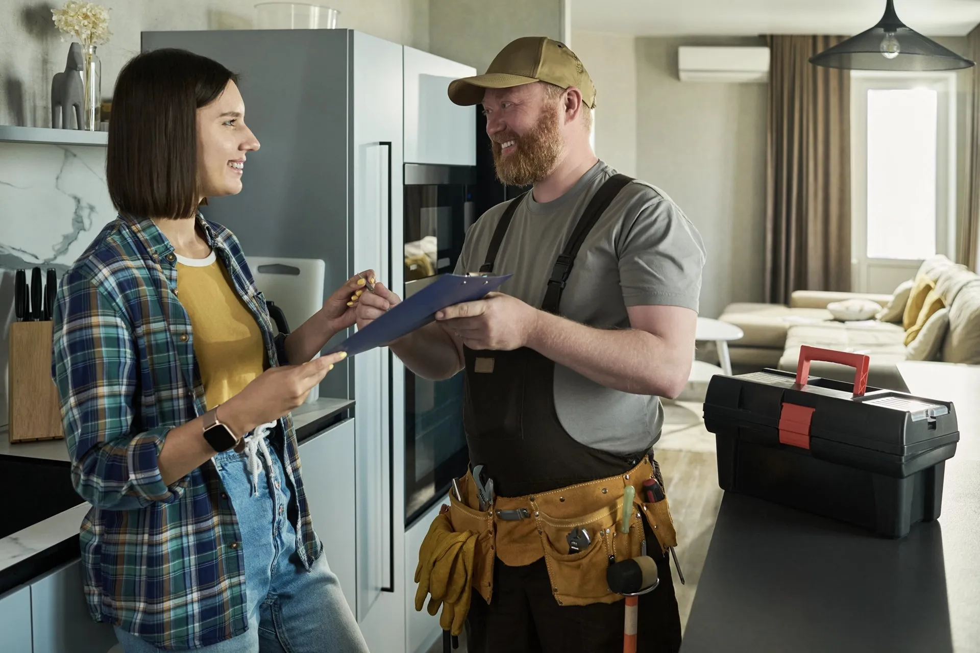 Handyman with a tool belt reviewing a repair checklist with a homeowner in her kitchen.