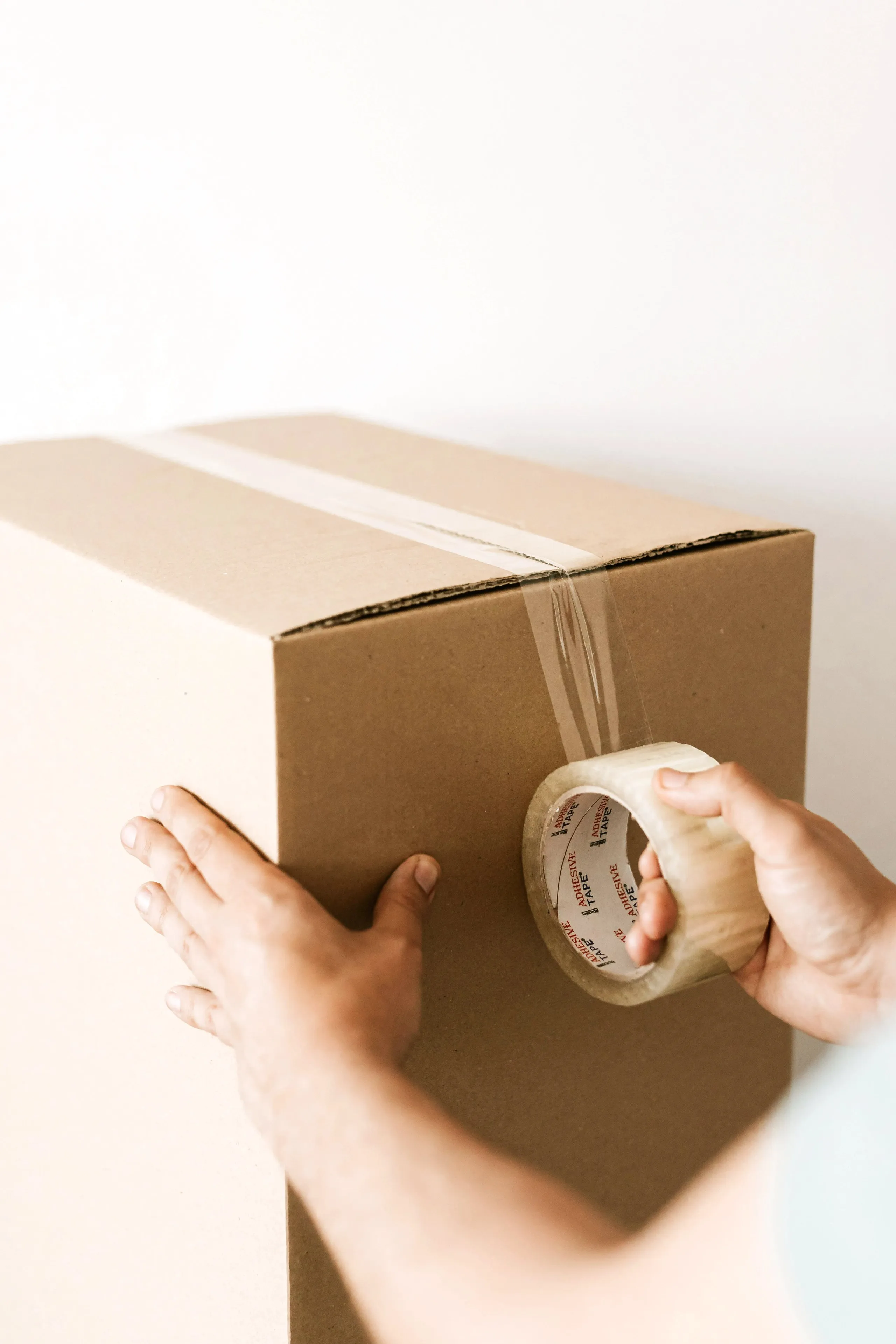 Hands sealing a moving box shut with packing tape.