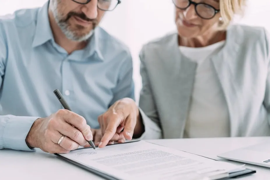 Close-up of a couple signing notarized documents together at a table.