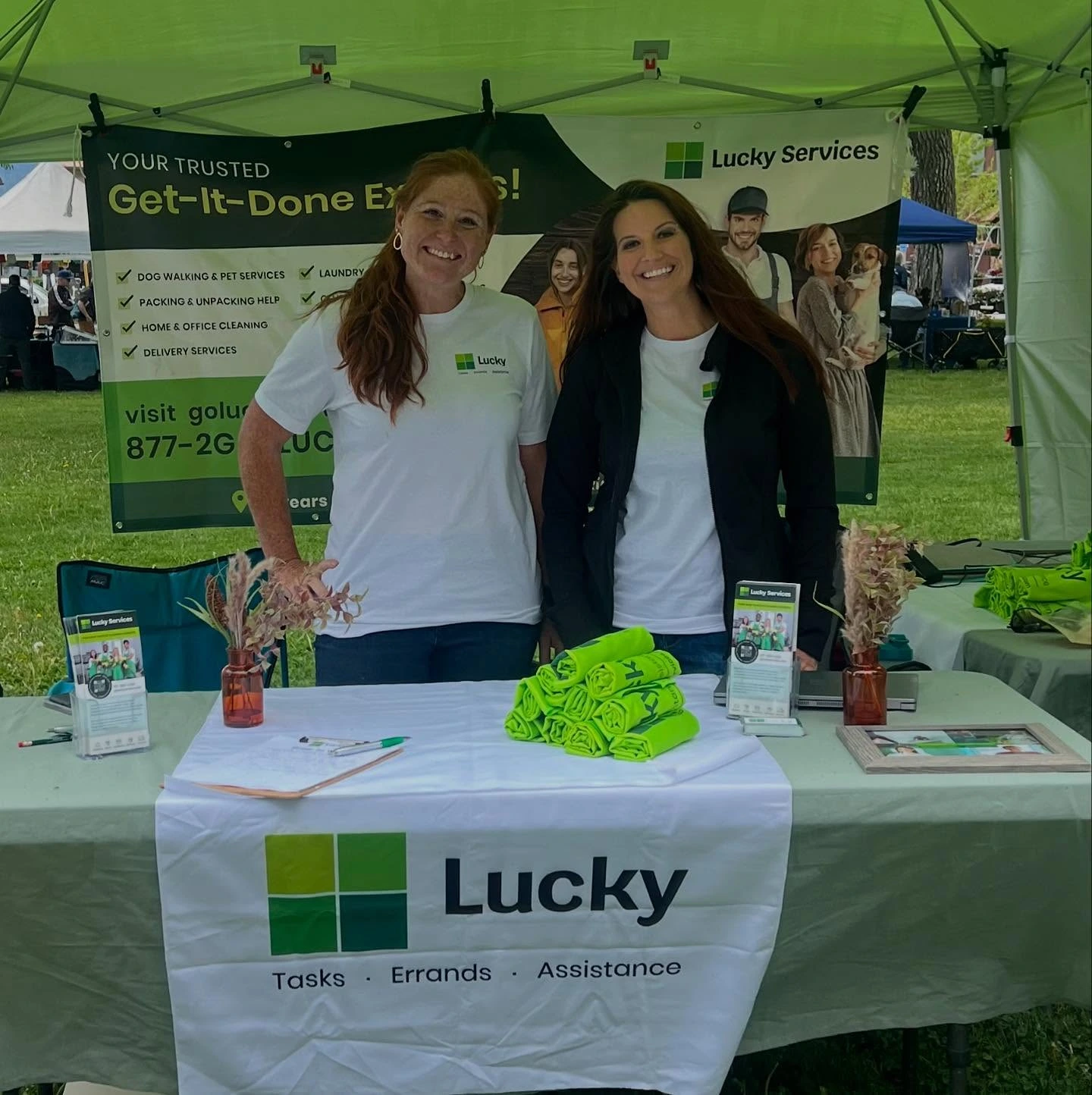 Jessika Loyer and Cheri Kurtz representing Lucky Services at the Ridgway Farmer's Market, standing at a booth promoting home cleaning, pet services, and errand assistance.