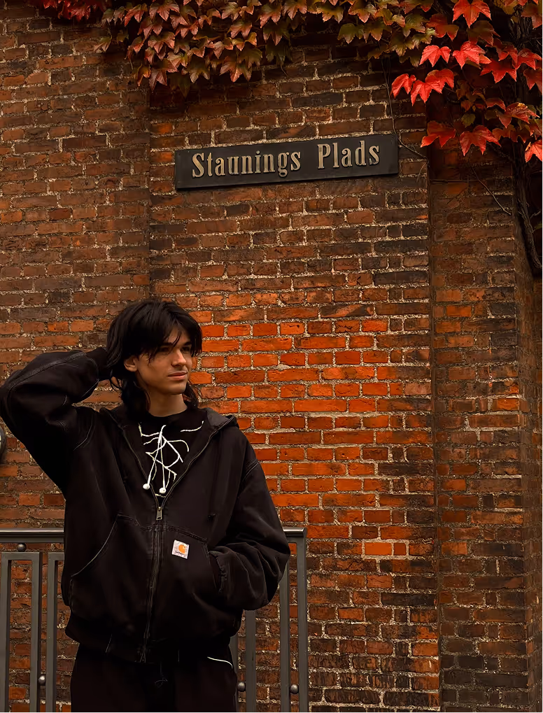 Yoan Samardzhiev, a Webflow Developer and UI/UX Designer, posing outdoors at Staunings Plads in front of a textured brick wall.