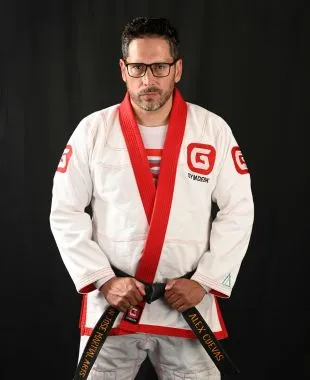 Man wearing a white and red Brazilian jiu-jitsu gi holding a black belt with his hands against a black background.