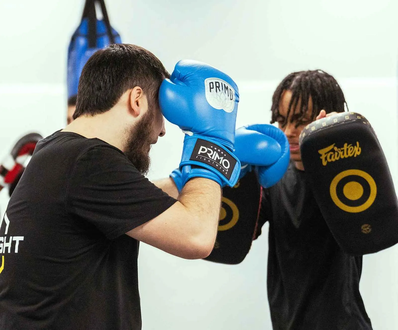 Boxer wearing blue gloves practicing punches on black and yellow focus mitts held by trainer.