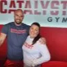 Two smiling people posing together in front of a red wall with 'Catalyst Gym' signage.