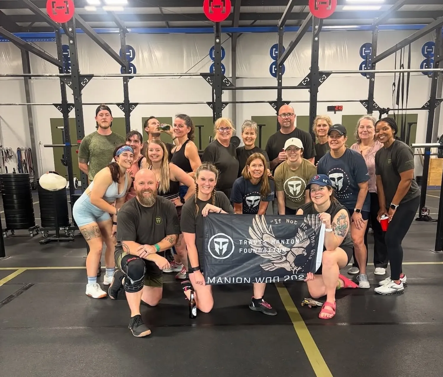 Group of smiling people posing in a gym holding a Trueles Manion Foundation banner.