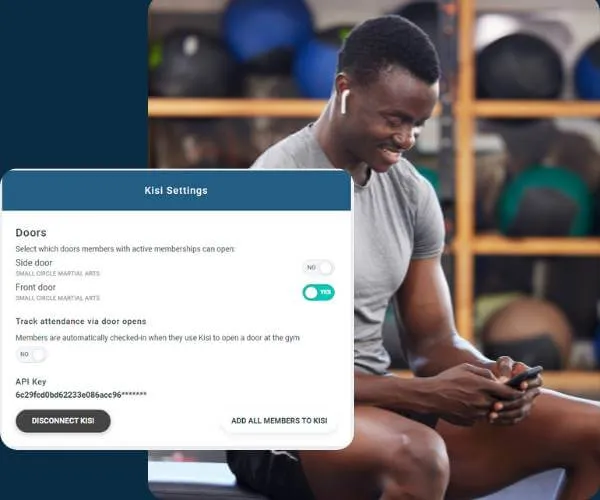 Smiling man in gray shirt wearing wireless earbuds, seated and using a smartphone in a gym with fitness balls in the background, with a Kisi Settings interface overlay about door access and attendance tracking.