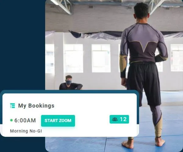 Man in athletic gear standing on a mat in a spacious gym with another person seated in the background wearing a mask, overlaid with a booking interface showing a 6:00 AM Morning No-GI Zoom class with 12 participants.