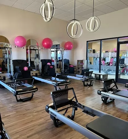 Pilates studio with reformer machines, wooden floor, pink exercise balls, and modern circular ceiling lights.