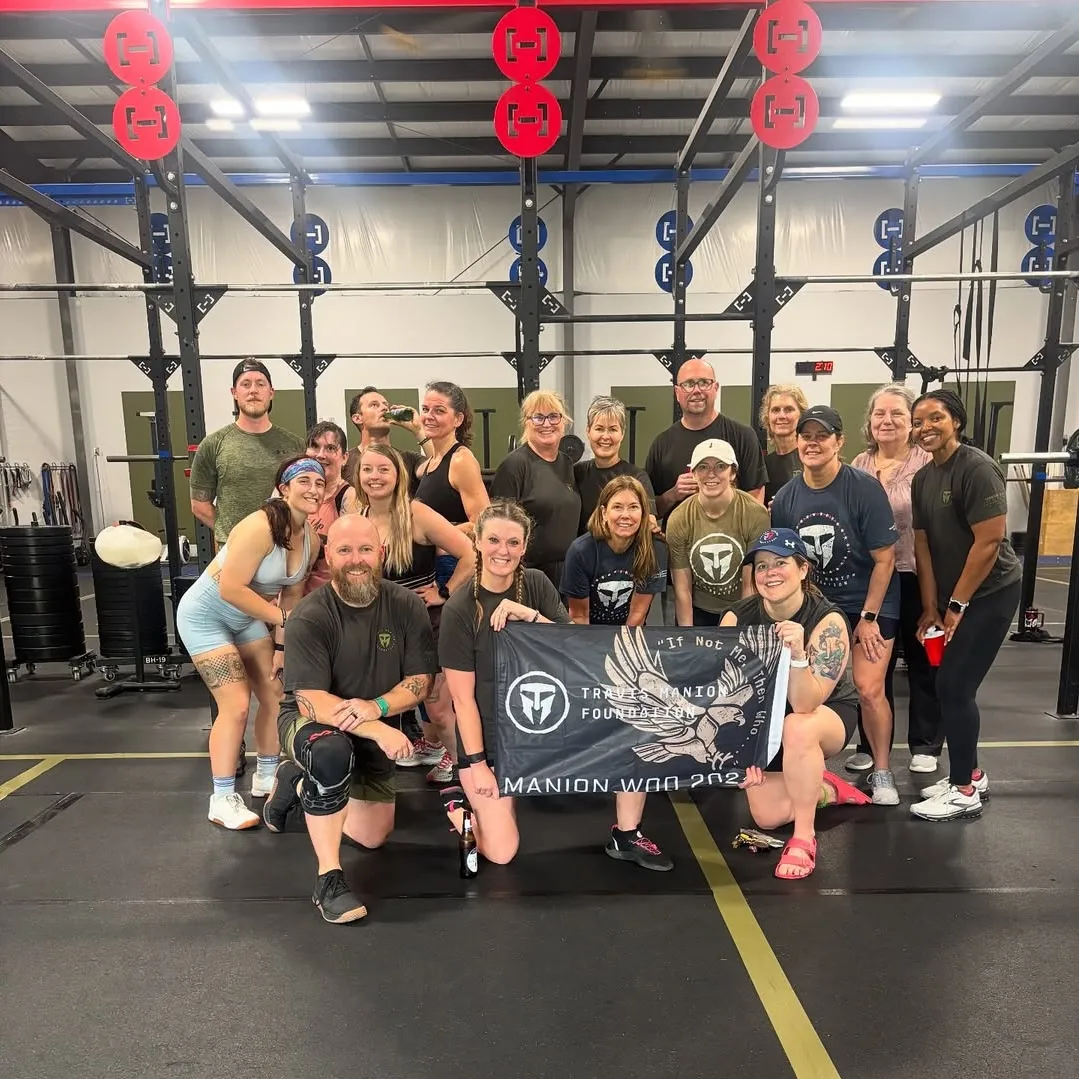 Group of 17 people posing inside a gym, holding a black banner with an eagle and text reading 'Travers Manion Foundation'.