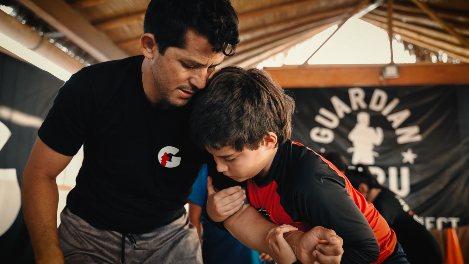 A Guardian Peru coach guides a young student through a jiu-jitsu technique.