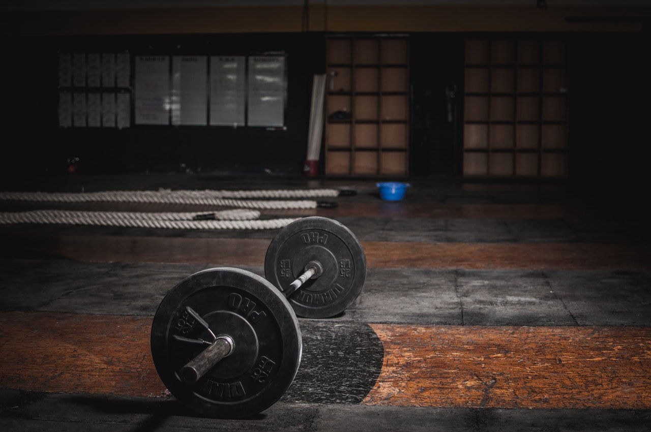 Loaded barbell sitting on the floor of an empty dark gym with battle ropes in the background
