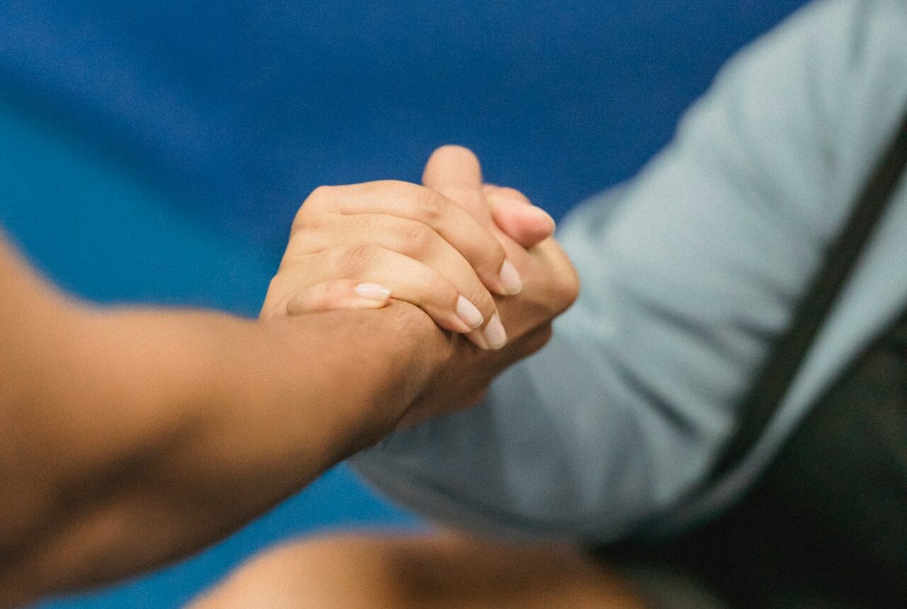 Close-up of two people clasping hands against a blue background