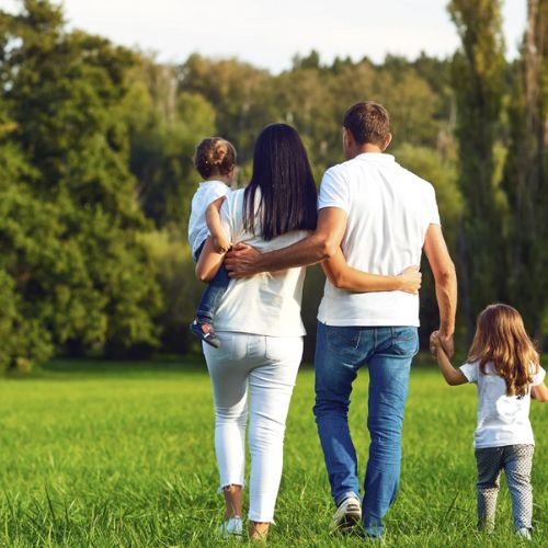 Family walking together in a green park from behind.