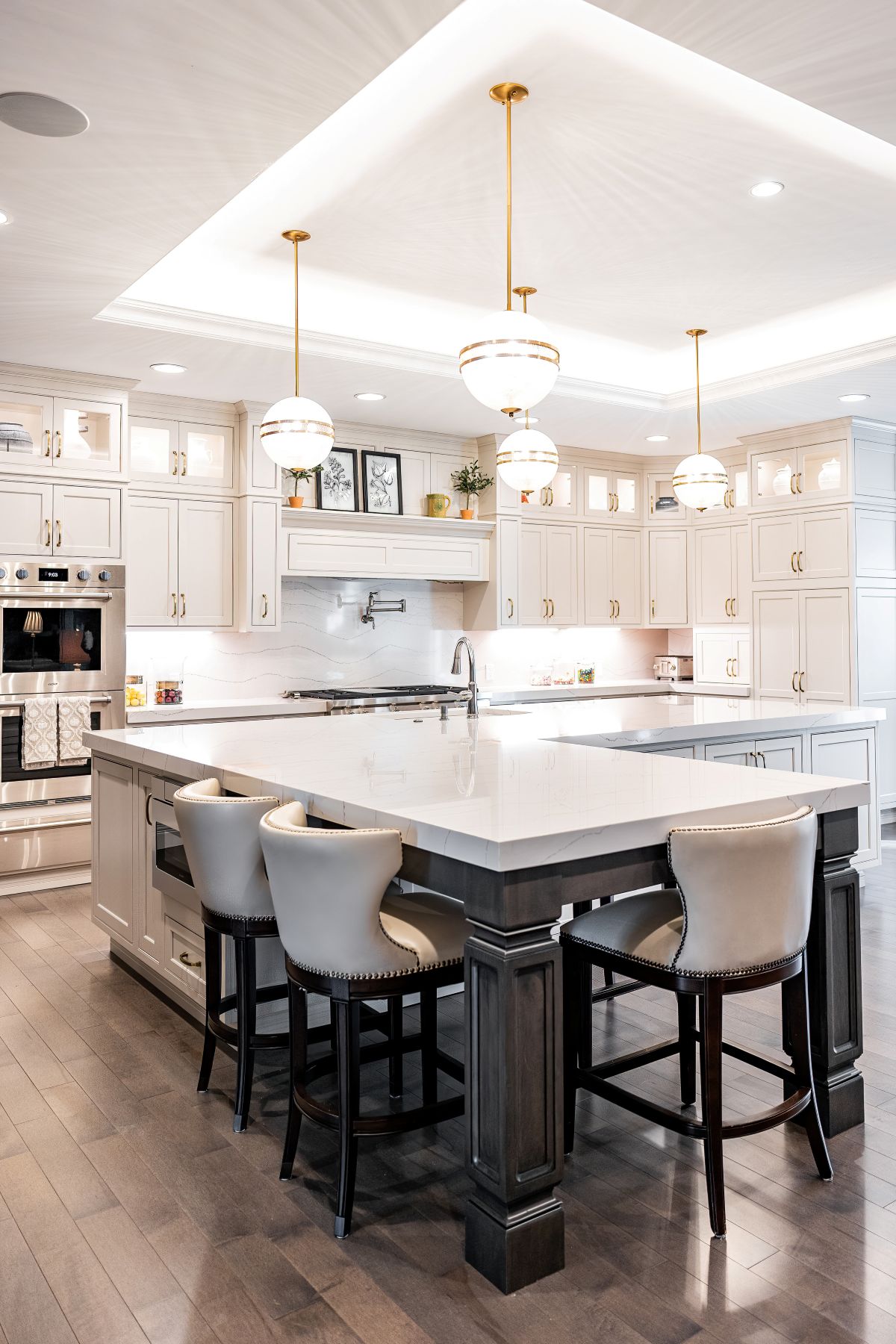 Bright modern kitchen with large marble island, three upholstered bar stools, white cabinetry, and gold pendant lights.