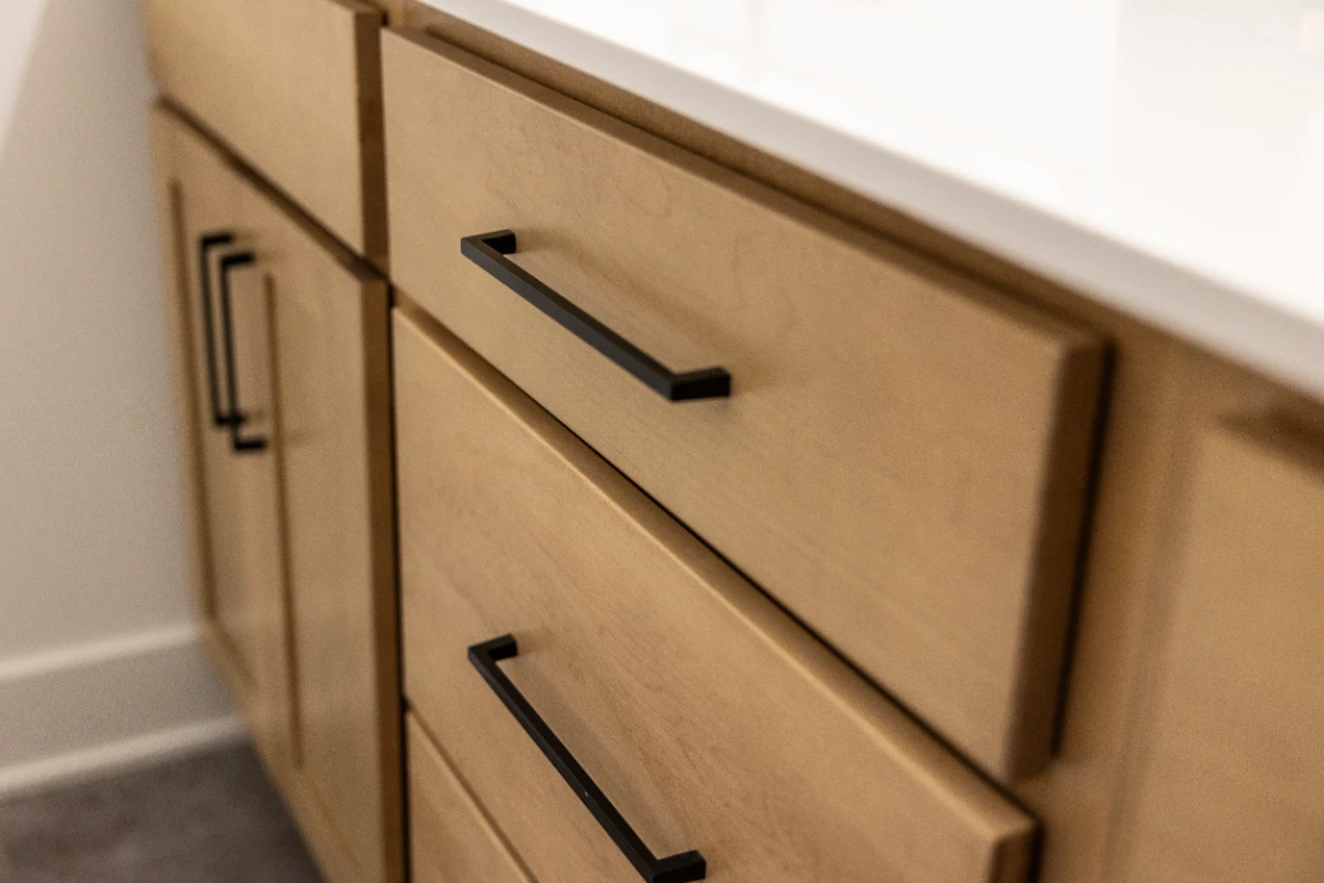 Close-up of light wood kitchen cabinets with black metal drawer handles under a white countertop.