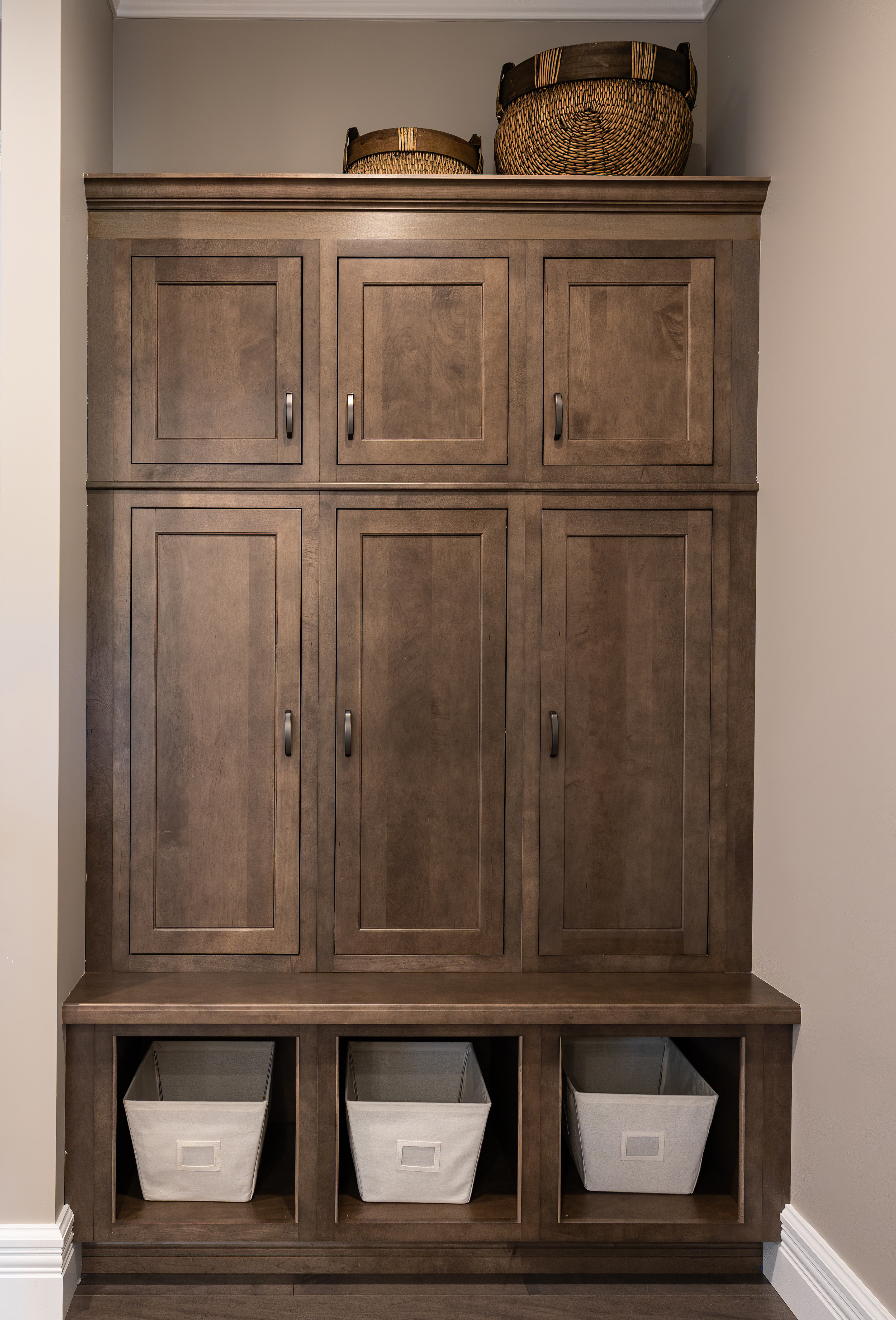 Tall wooden storage cabinet with six doors, three fabric bins at the bottom, and two woven baskets on top.