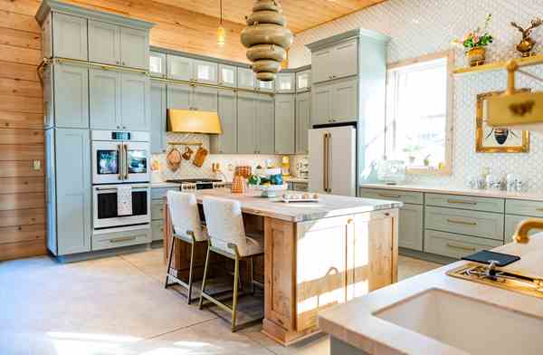 Bright kitchen with light gray cabinets, a wooden island with two chairs, stainless steel appliances, and a window letting in natural light.
