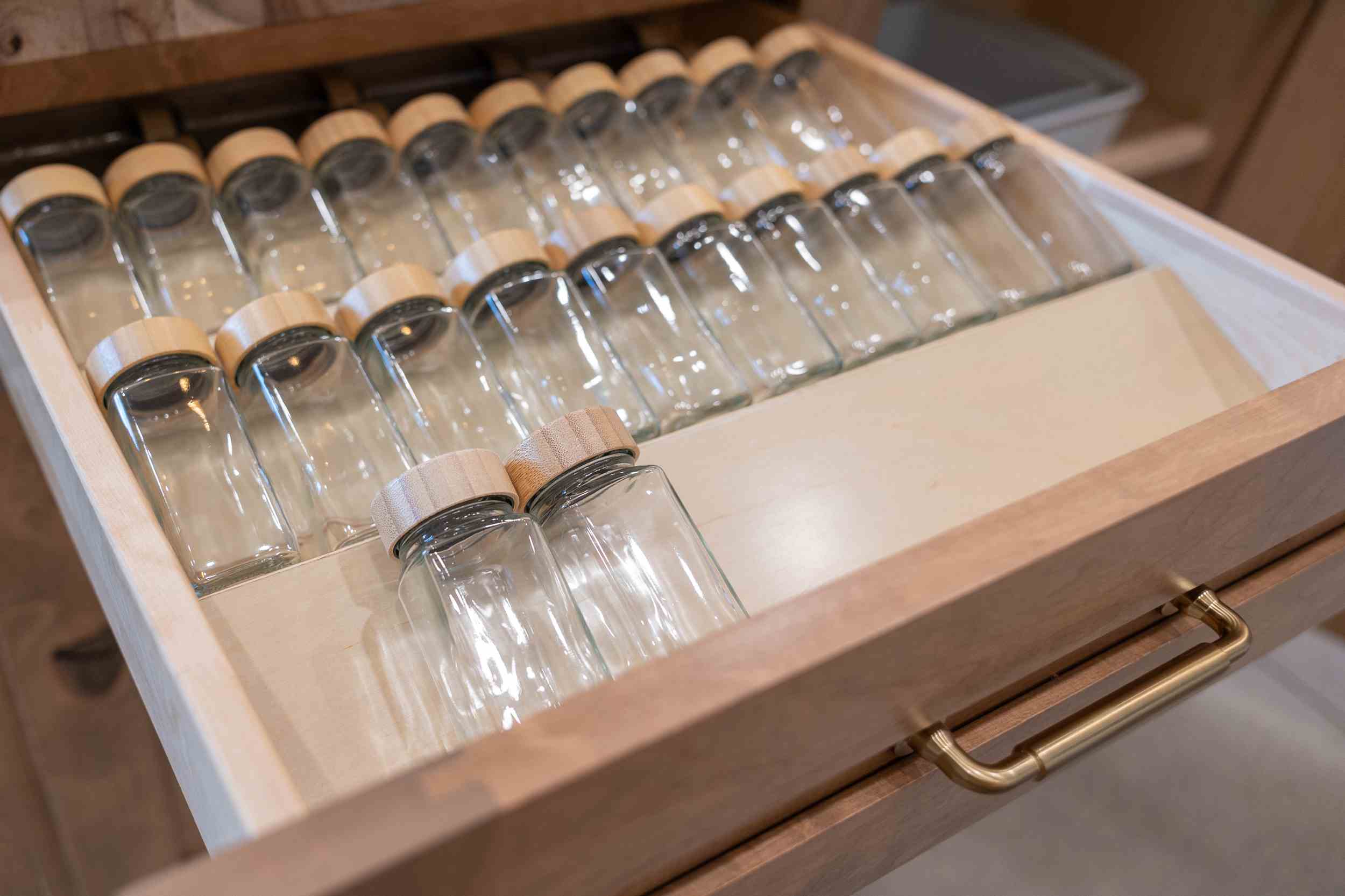 Open wooden drawer containing empty glass jars with wooden lids neatly arranged.