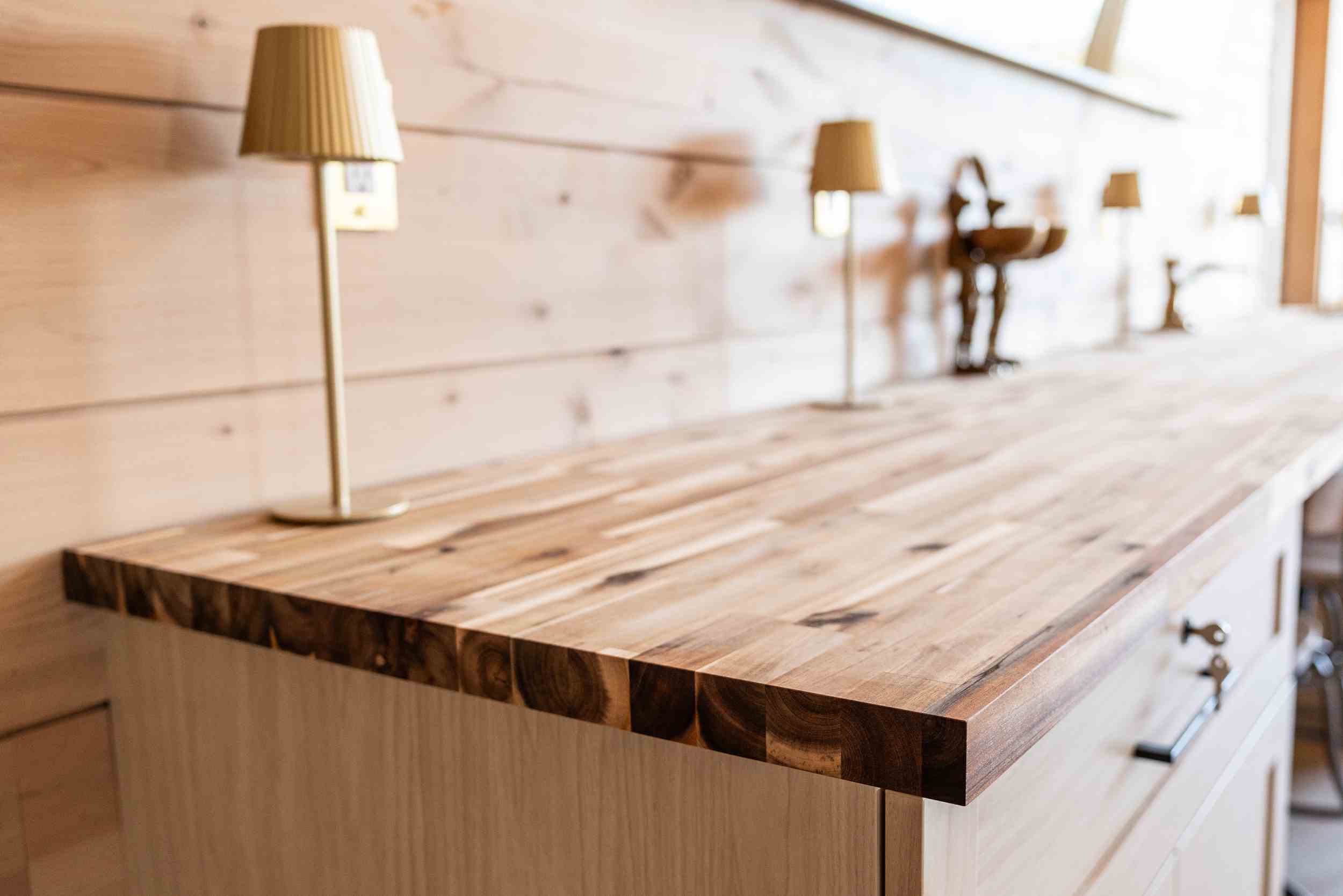 Close-up of a polished wooden countertop with small table lamps and wooden wall paneling in the background.
