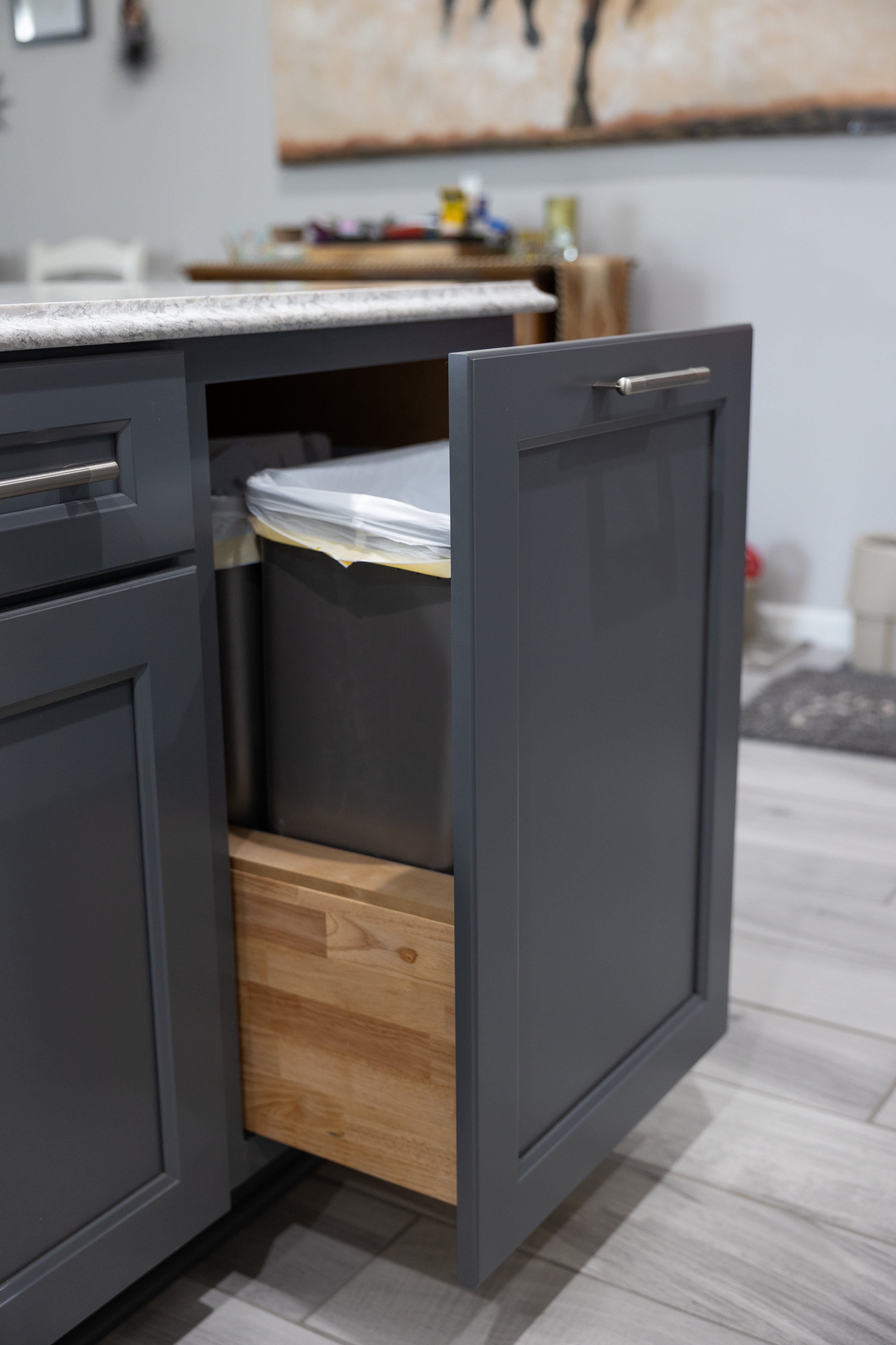 Gray kitchen cabinet door opened revealing a pull-out trash bin with a white liner inside.